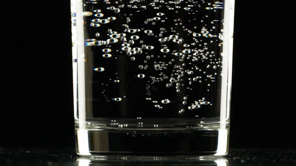 Close Up Footage of Bottom of Glass with Clear Sparkling Water Standing on Black Background in alt