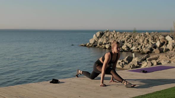 Sporty Flexible Woman Is Doing Longitudinal Split Sitting on Pier Near River.