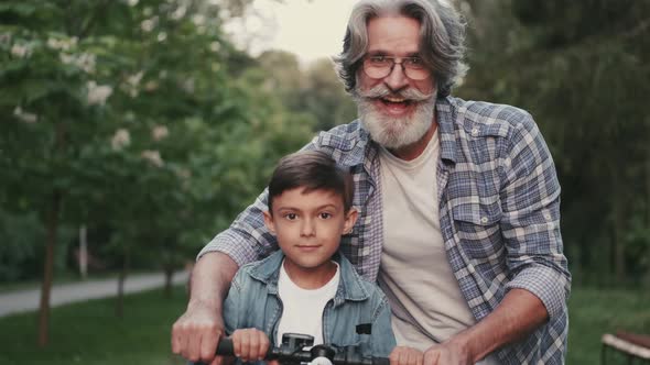 Smiling Boy on a Bike and Hippie Grandfather Standing in a Park alt