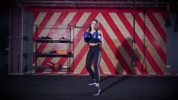 Young Woman in Boxing Gloves Prepares for a Fight and Makes Several Blows to the Camera