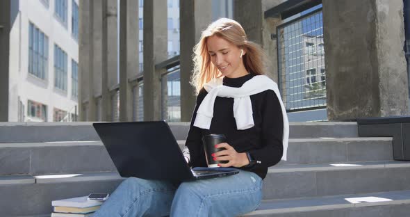 Young Woman in Casual Clothes which Sitting on Steps of City Building, Working on Laptop alt