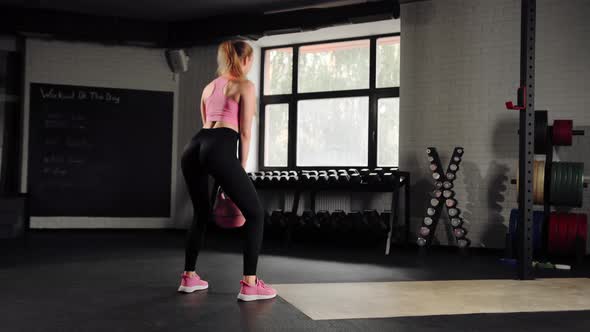 Attractive young beautiful woman doing cardio exercise and squatting with kettlebell in gym alt
