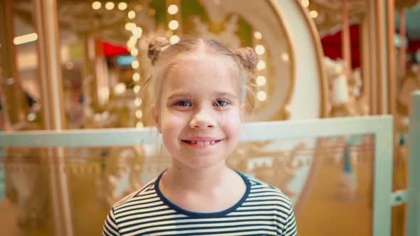 View of Blond Girl Looking at Camera Against the Background of Glowing Carousel
