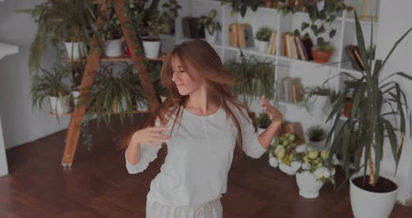 Young Girl in Pajamas is Having Fun in a Bright Room with Green Plants Dancing and Spinning