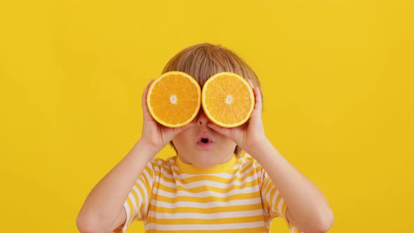 Surprised child holding halves of orange fruit like a sunglasses. Slow motion