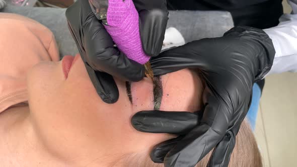Beautician in Gloves Makes Permanent Makeupof the Eyebrows to a Young Women