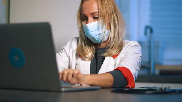Side View Modern Female Doctor in Medical Mask Typing Recipe Using Laptop alt