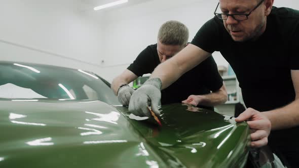 Two Men are Vinyl Wrapping a Car in Dark Green Color Using Plastic Cards