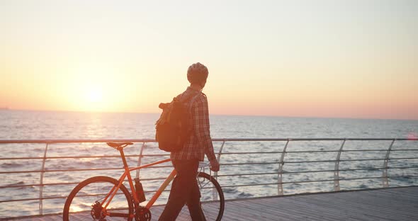 Authentic Creative Shot of a Man with Bicycle Walking at Sunrise on Sea Embankment alt