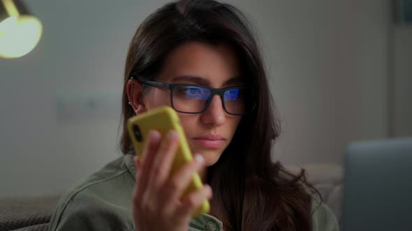 Girl Communicates on a Mobile Phone with a Smile on Her Face While Sitting at a Laptop