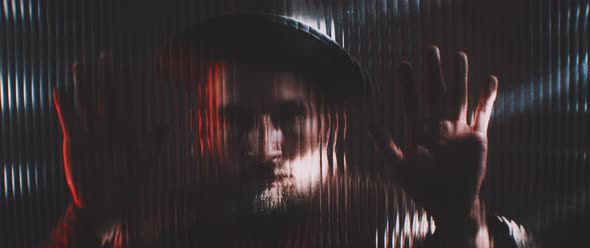 Man in shutter lights looking through clear panel holding hands up alt