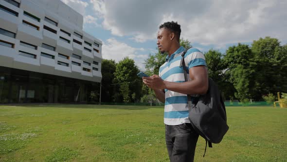 Handsome Afroamerican Man Using Smartphone on the Background of the University alt