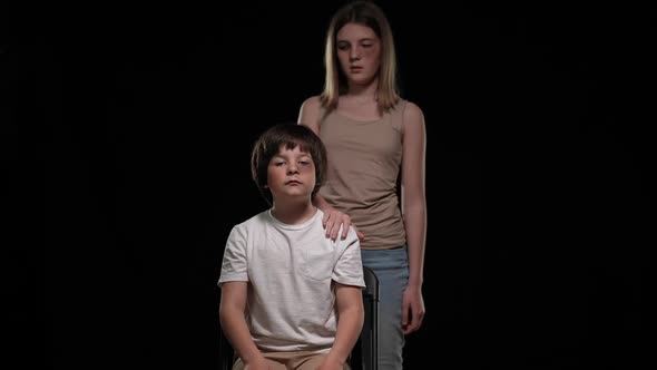 Unhappy Bruised Abused Boy Sitting on Chair Touching Girl Hand on Shoulder Looking at Camera alt