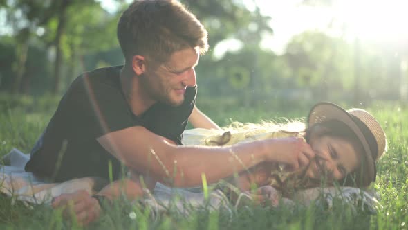 Joyful Man Laughing Tickling Girl Lying in Sunbeam on Spring Summer Lawn in Park alt
