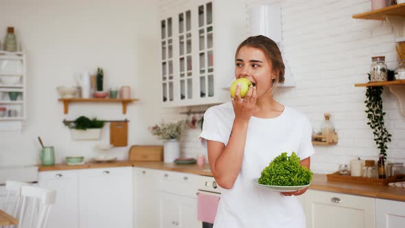 Girl Smiling Eating Apple and Holding Lettuce Salad Leaves on Plate alt