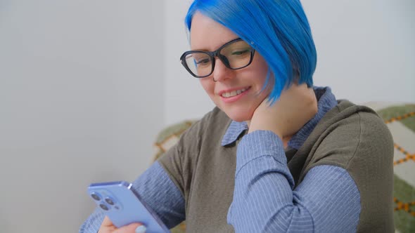Cute white girl with blue hair browsing internet and social media on modern smartphone in 4k alt