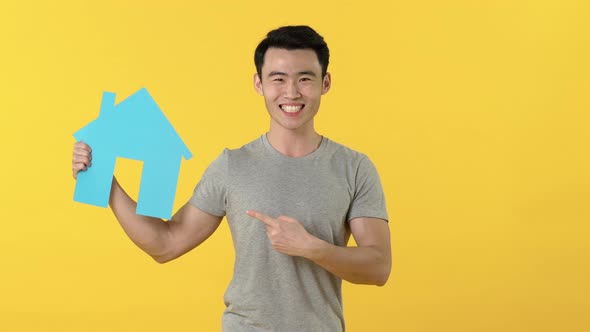 Excited Asian man in gray t-shirt presenting home sign for real estate concept