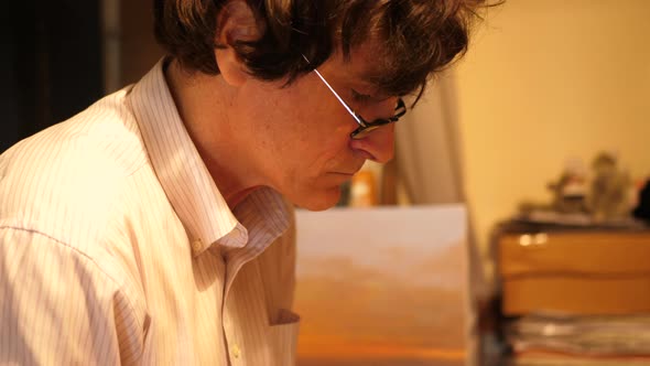 An artist paints an oil painting on canvas inside his art studio. alt