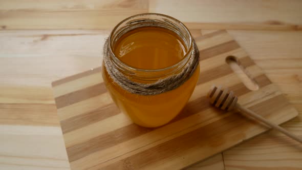 Golden Honey in a Glass Jar and a Spoon on a Wooden Board
