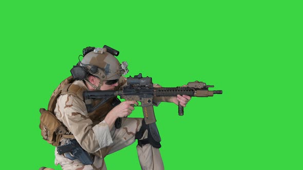 Paratrooper in Uniform Shooting From Sitting Position on a Green Screen, Chroma Key. alt