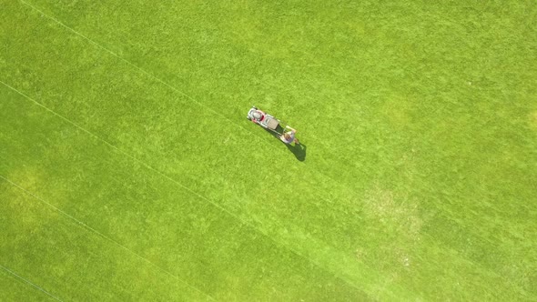 Aerial View of Small Figure of Man Worker Trimming Green Grass with Mowing Mashine on Football alt