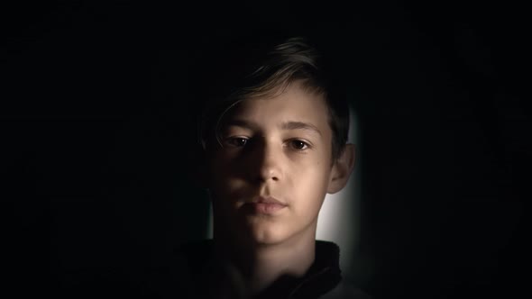 Portrait of a Serious Boy Looking at the Camera in the Dark Moving Camera alt
