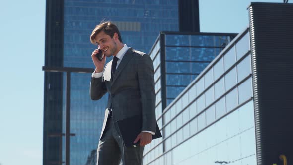 Businessman, Top Manager in a Suit Stands Near a Glass Skyscraper and Talking on a Mobile Phone alt