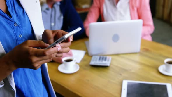Woman text messaging on mobile phone in cafeteria alt
