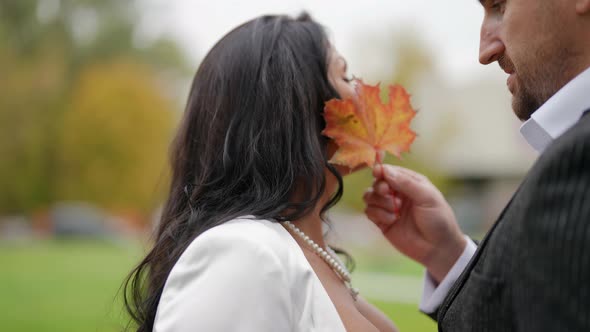 Man is Stroking Face of His Beloved Woman By Maple Leaf During Walk in Autumn Park alt