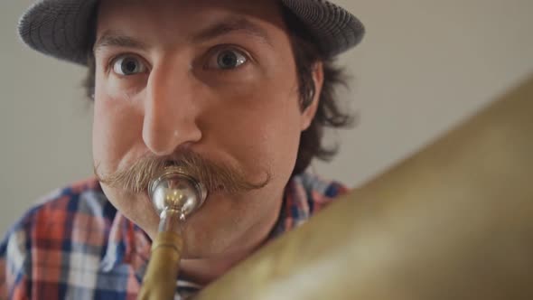 Cheerful Young Man with a Funny Mustache and a Hat Playing on the Big Tuba