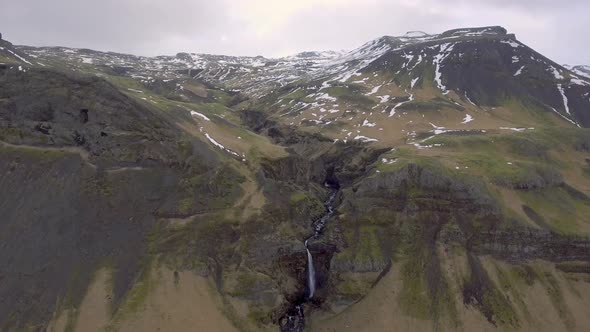 Aerial view of waterfall in Iceland with snowy mountains on background