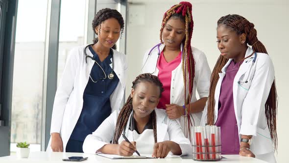Young Doctors Have a Discussion Standing at a Table While One of Them Makes Notes alt