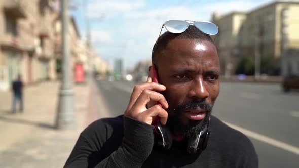 Close-up of an African-American Man Arguing on a Smartphone in a Modern City Against the Background alt