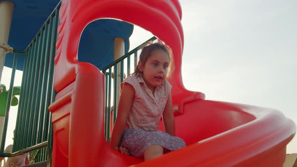 Cute Little Girl Slides Down the Slide at the Playground in Summer alt