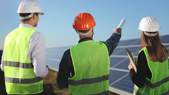Three Engineers are Standing and Looking at the Solar Panel Station alt