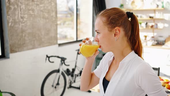 Young Lady Drinking Orange Juice From Glass While Standing in Kitchen at Home alt