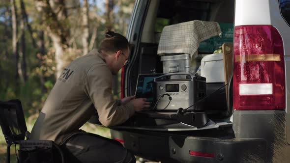 digital nomad sitting down at trunk lid to work on his computer alt