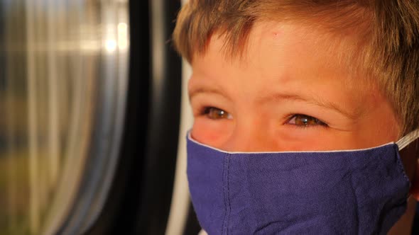Boy Looking in the Window During Train Ride. Close-up of Kid in Cotton Facemask. Sun Light on the