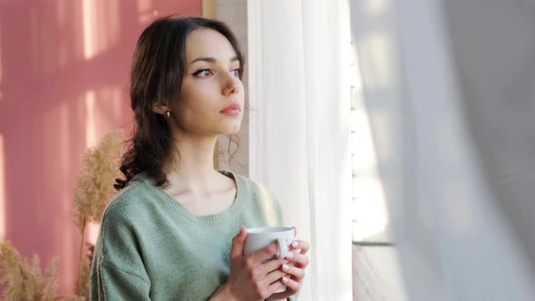 Beautiful Woman Sitting Near Window and Enjoy a Cupt of Tea Admiring Sunrise alt