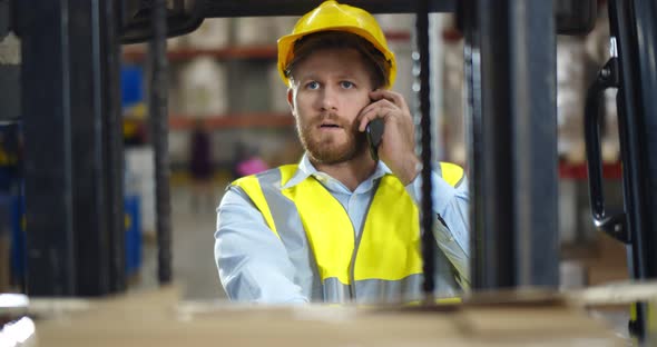 Industrial Warehouse Manager Sitting in Forklift Truck and Having Phone Call alt