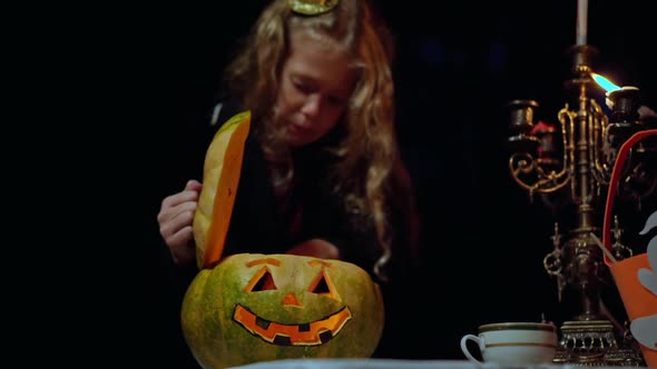 Halloween Pumpkin with Light Inside on Table in Night Forest with Blurred Little Girl Opening alt