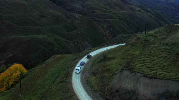 Cars drive along empty mountain road and disappear behind the mountain