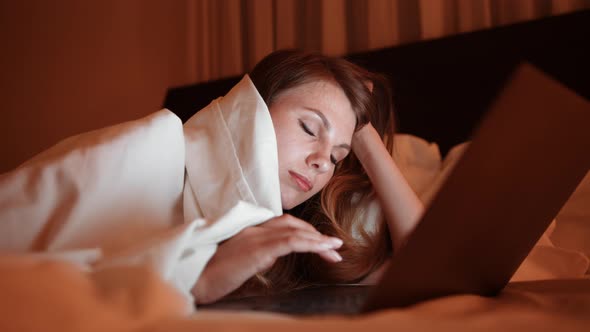 Young Woman Falling Asleep While Using Laptop in Bed alt