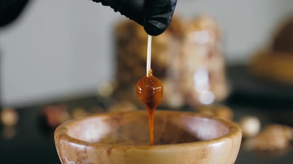 Pastry Chef is Dips a Hazelnut in Caramel for Making Topping for a Cake