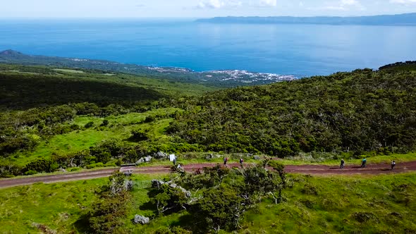 Sliding Shot of people walking on a dirt road. View of Sao Roque do Pico village in the background. alt