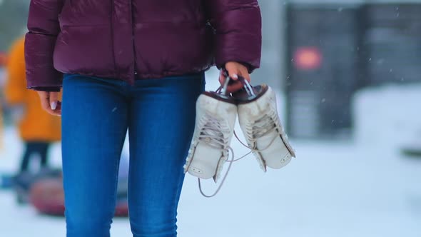 Lady in Jacket Walks Carrying Skates Along Snowy City Park