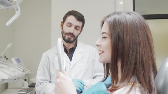 Dentist Talking to Patient While She Looks in the Mirror After Dental Treatment alt