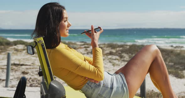 Caucasian woman lying on a beach buggy by the sea talking on smartphone alt