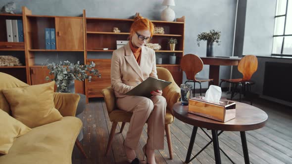 Redhead Female Psychologist Taking Notes and Posing for Camera at Work alt
