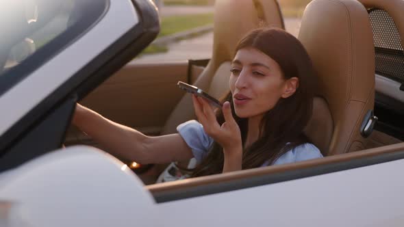 Beautiful Stylish Woman Sits in Her Luxury White Convertible and Sends Voice Message Via Smartphone